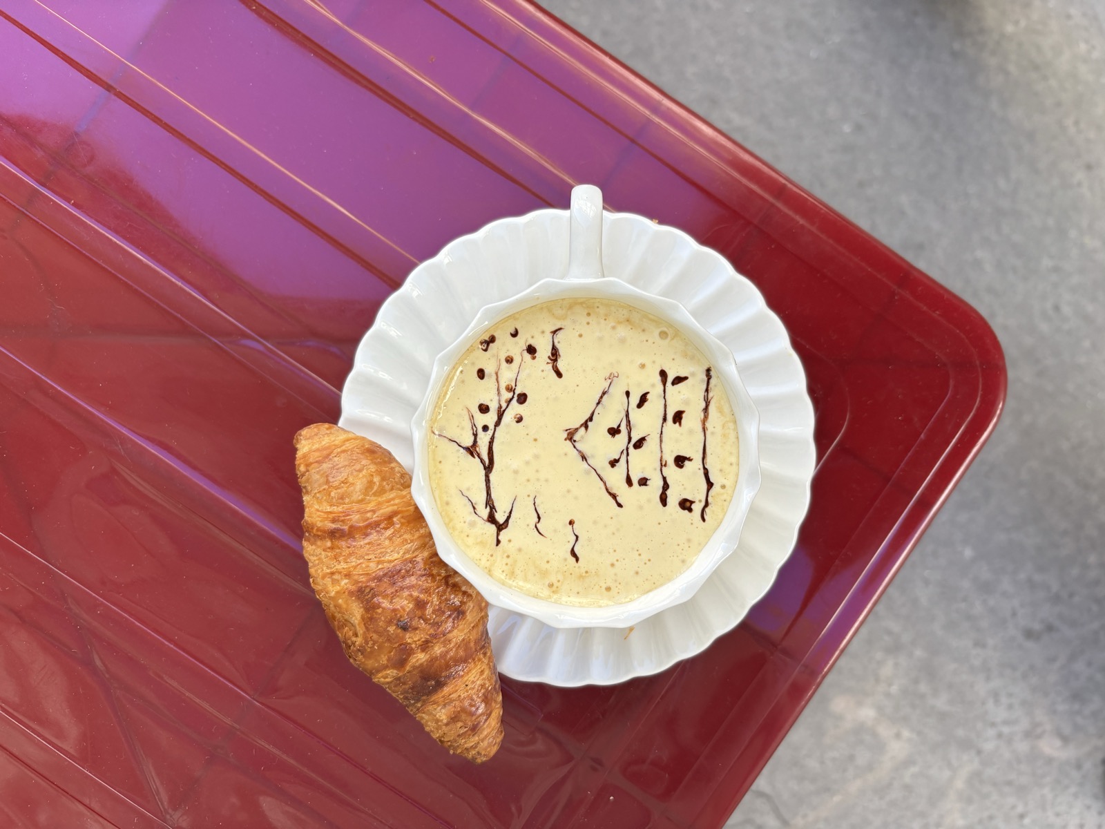Un café à la crème accompagné d’un croissant sur une table rouge